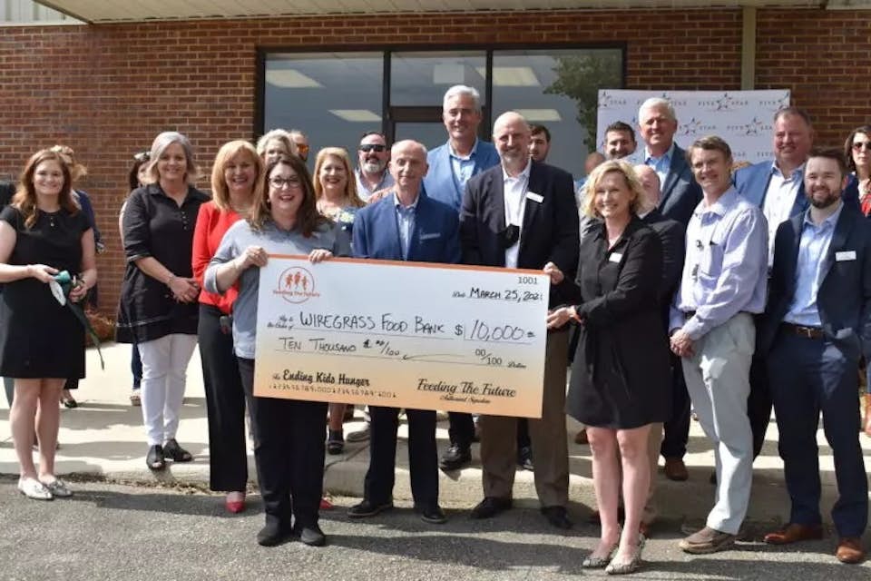 Group of people holding a big check outside of a building