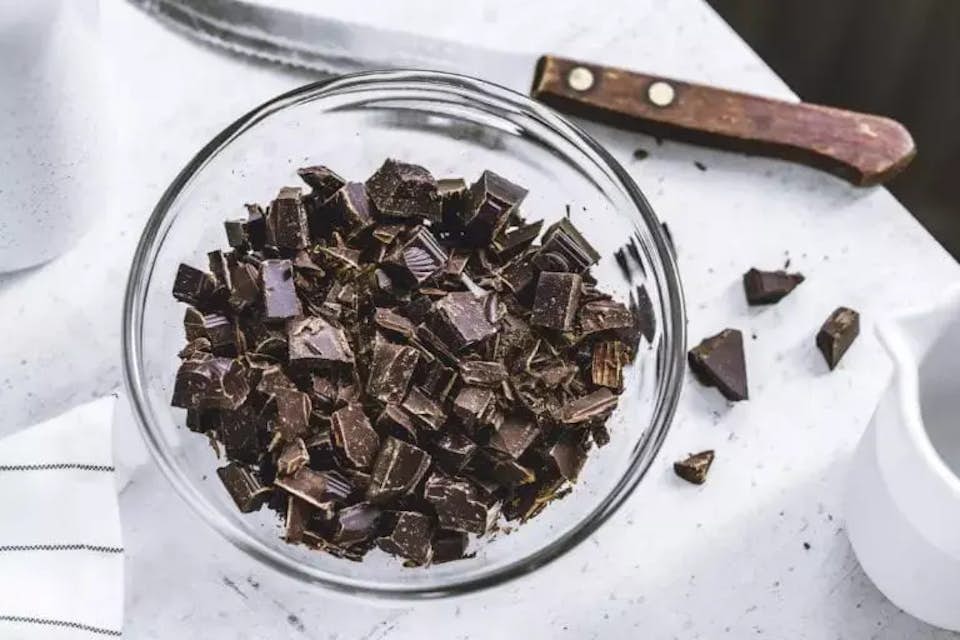 Chunks of dark chocolate in a bowl next to a knife